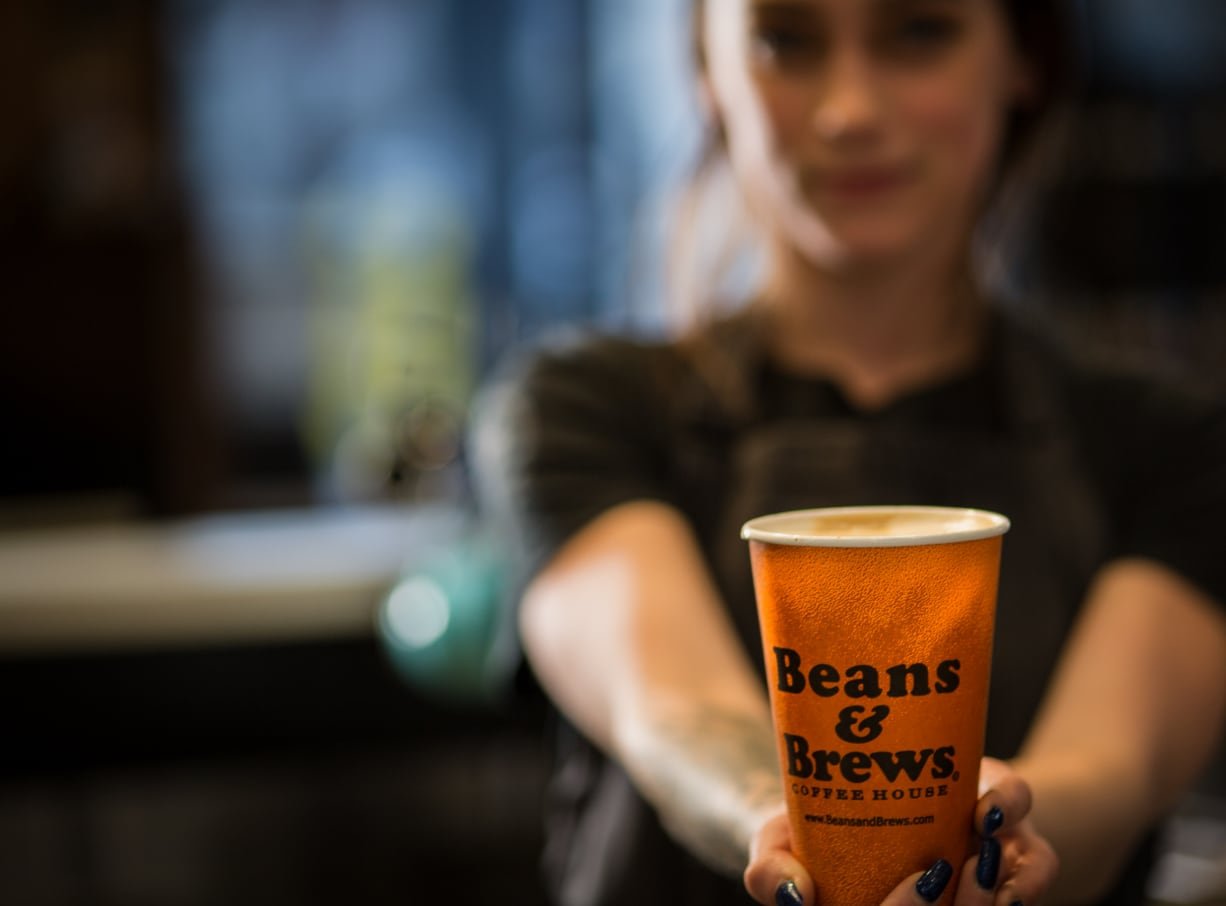 Bean & Brews employee holding a cup of coffee