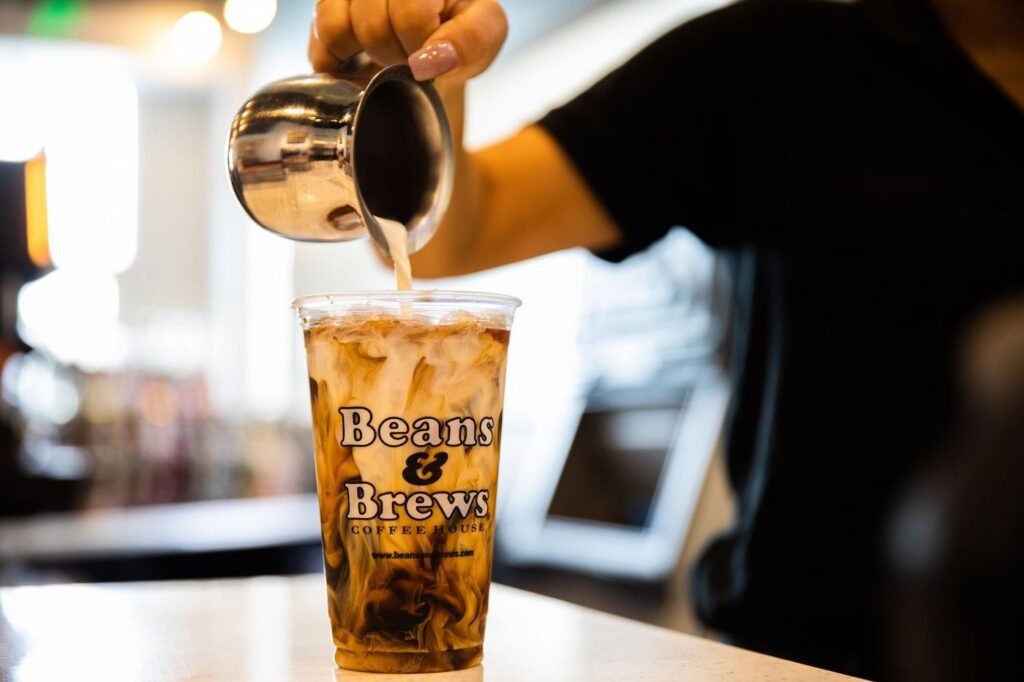 Beans and brews employee pouring creamer into cold brew coffee cup